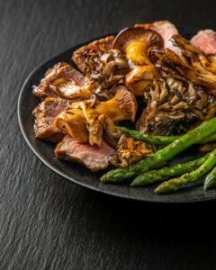 Dish with mushrooms, asparagus, and possibly bacon on a dark surface