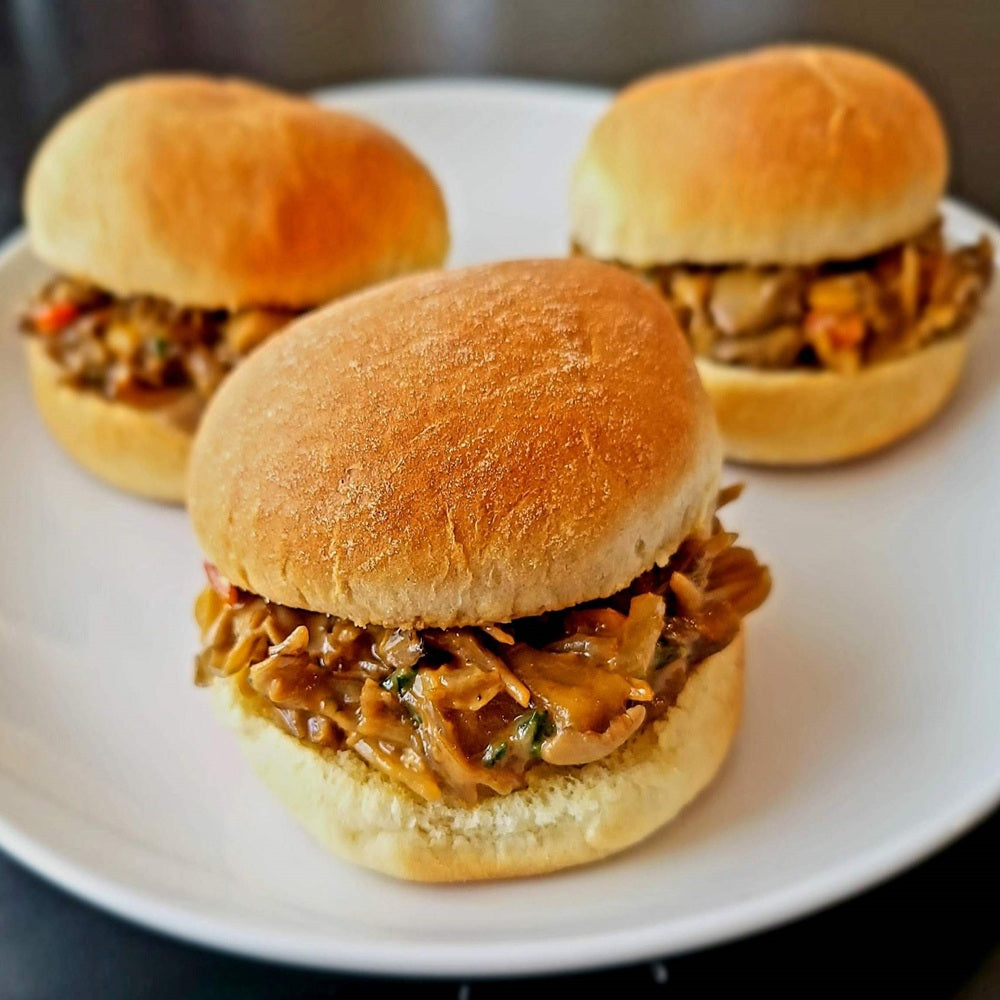 Three sliders with pulled meat on buns on a white plate.